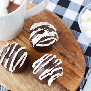 Hot chocolate bombs on a board next to a mug of hot cocoa and marshmallows.