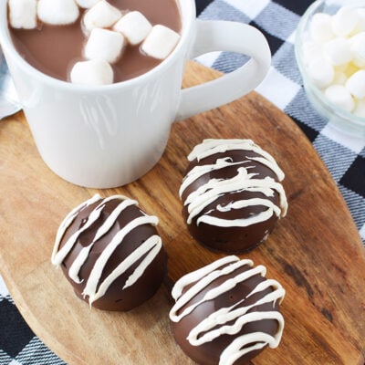 Three hot chocolate bombs on a board next to a mug.