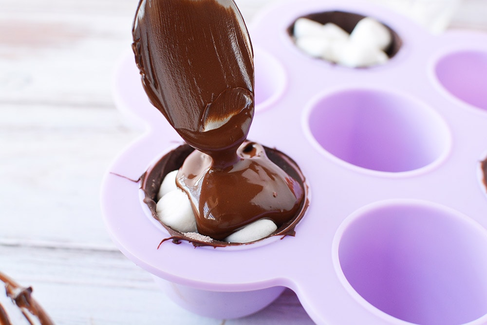 Putting melted chocolate over marshmallows in candy mold.