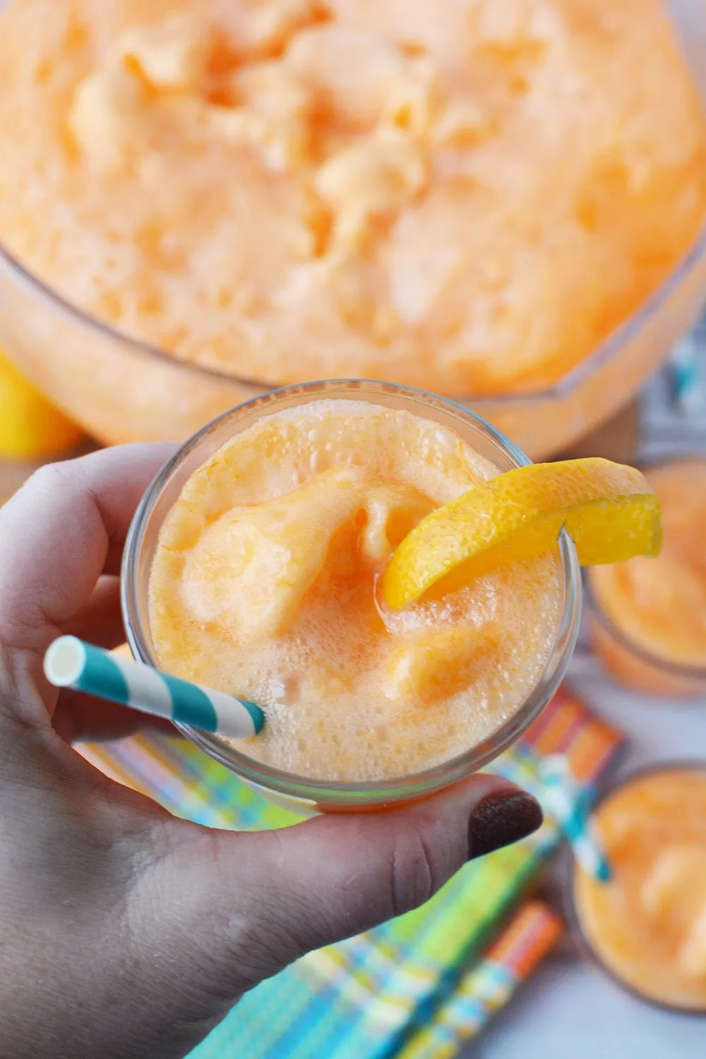 Holding up a glass of orange punch with an orange slice above bowl.