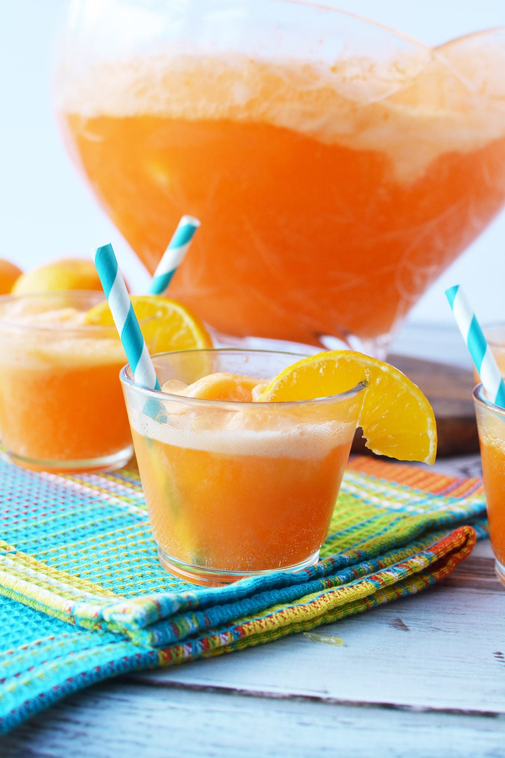 Glass of punch with bowl filled with orange punch.