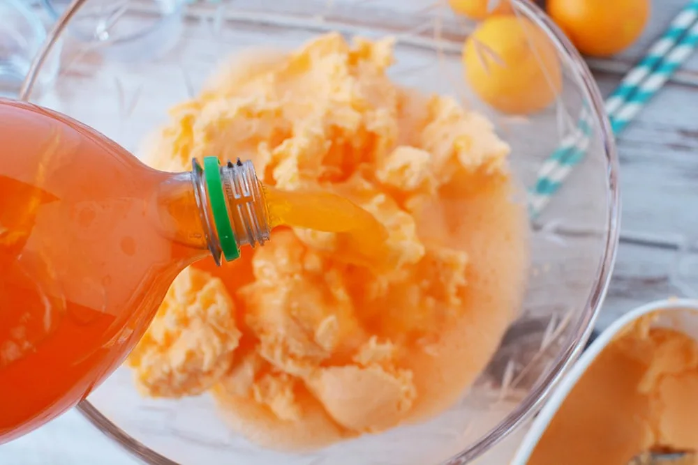 Pouring orange soda into punch bowl with sherbet. 