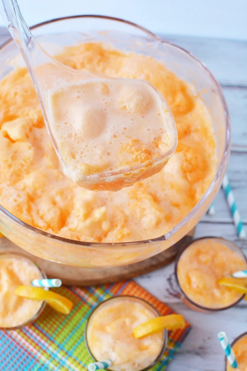 Ladle full of orange sherbet punch above punch bowl.