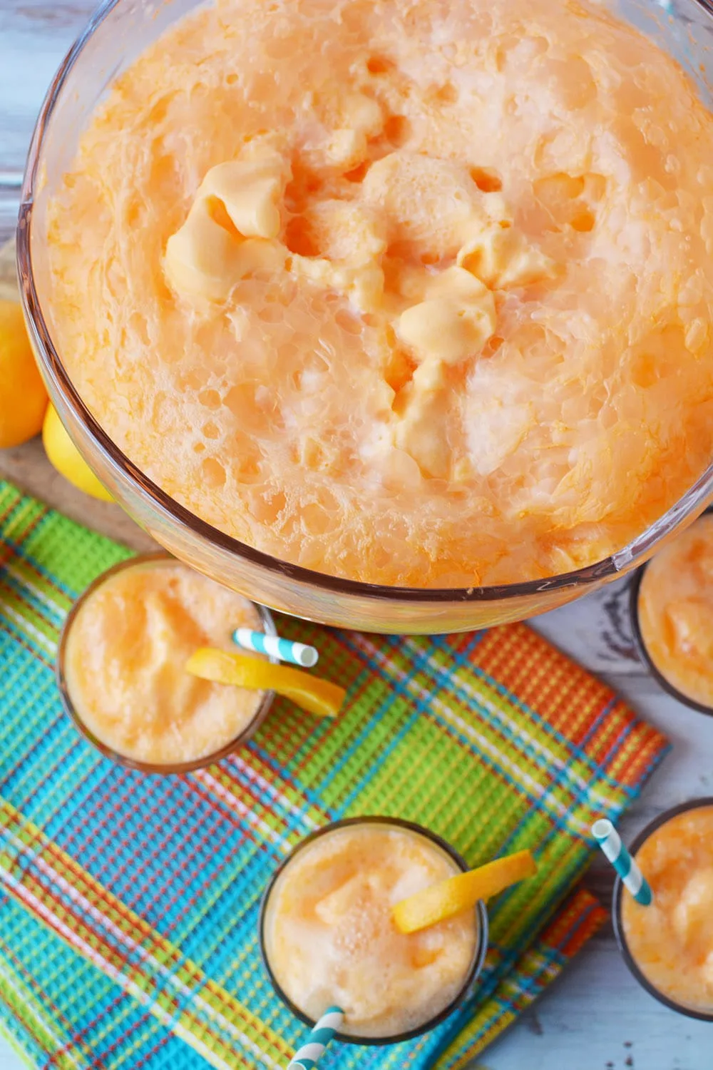 Punch bowl filled with orange sherbet punch with glasses around it. 