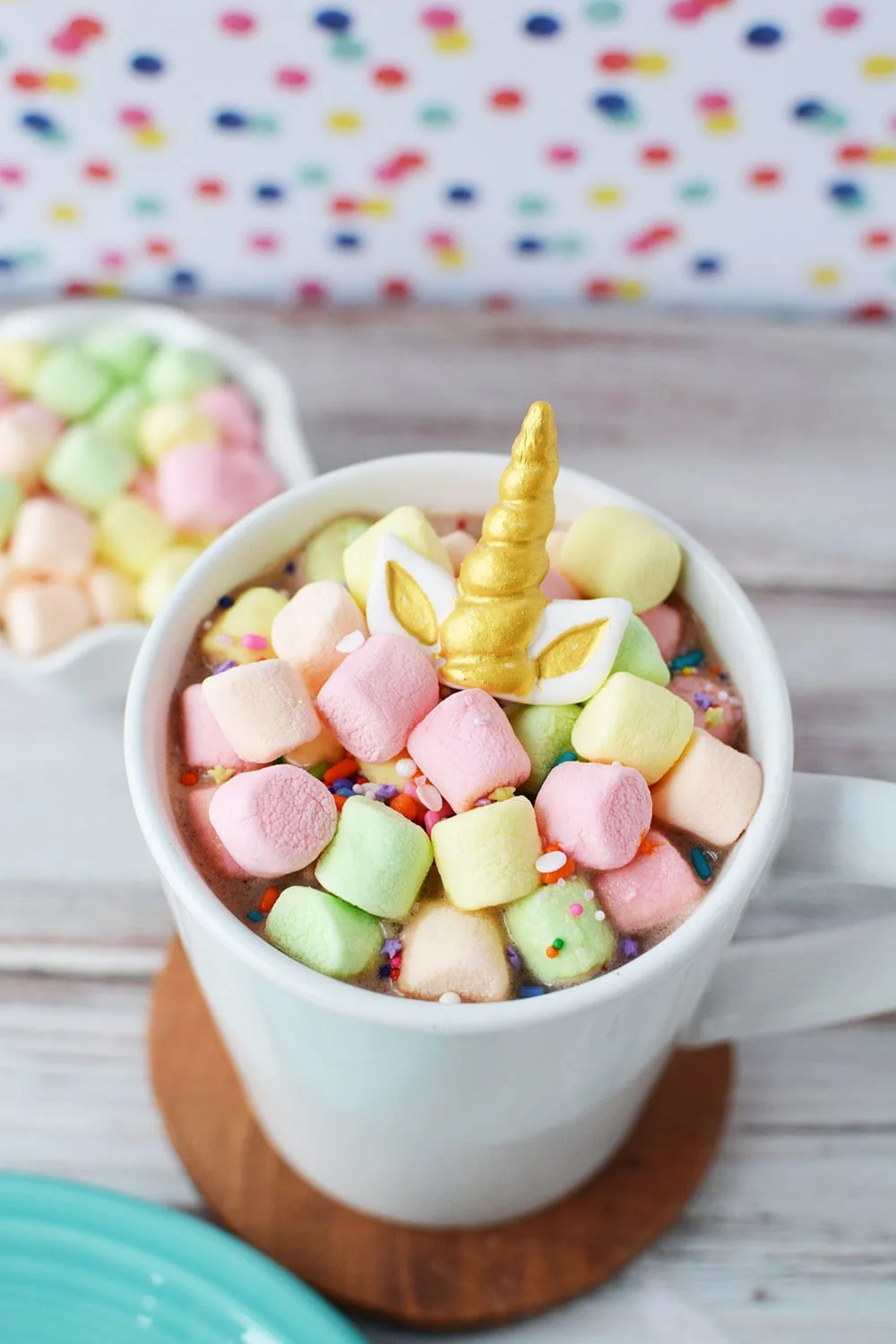 Hot chocolate in a mug topped with colored marshmallows and a gold unicorn horn.