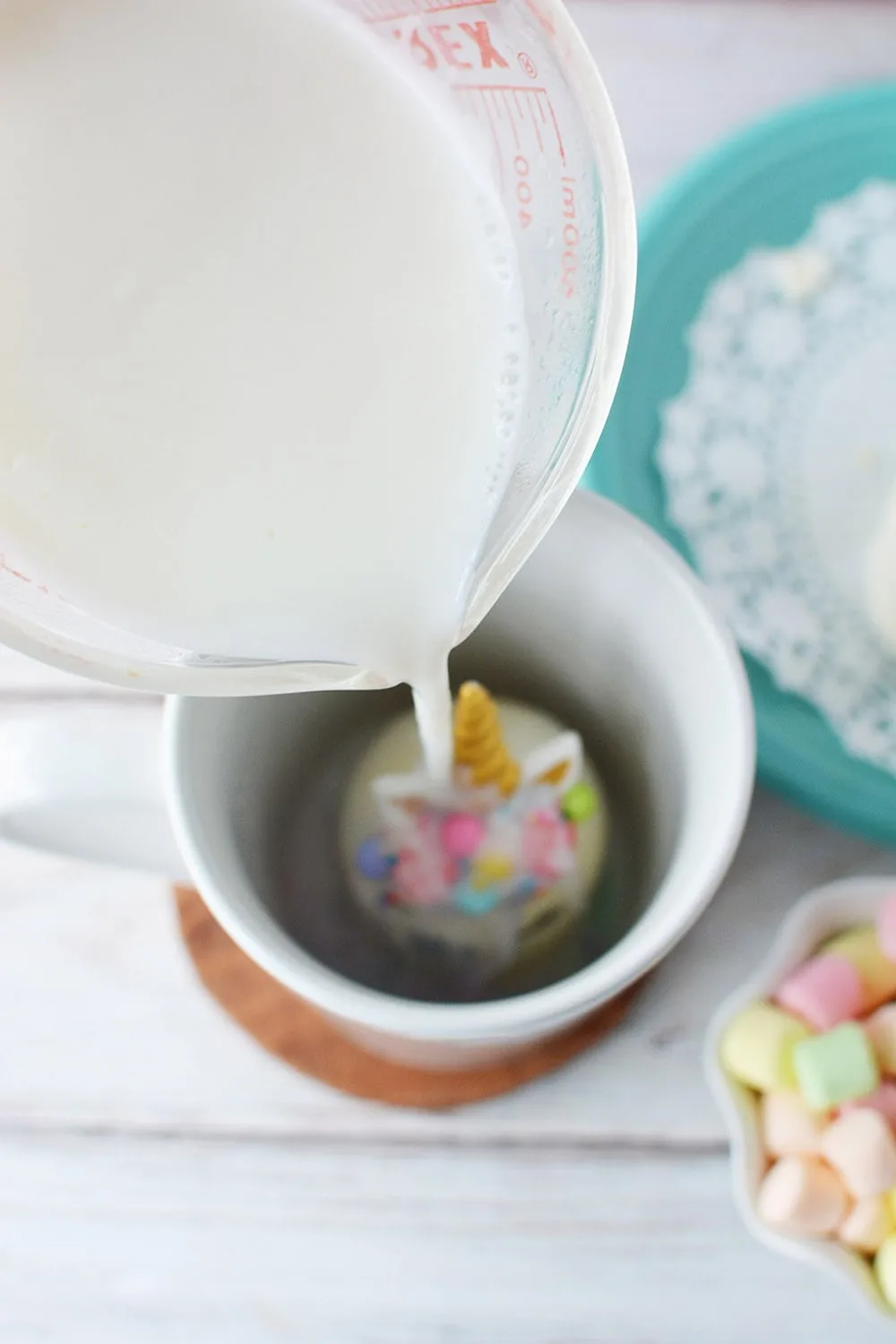 Pouring hot milk onto unicorn hot chocolate bomb in mug.