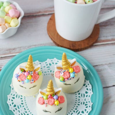 Unicorn hot chocolate bombs on a blue plate buy finished hot chocolate with colored marshmallows.