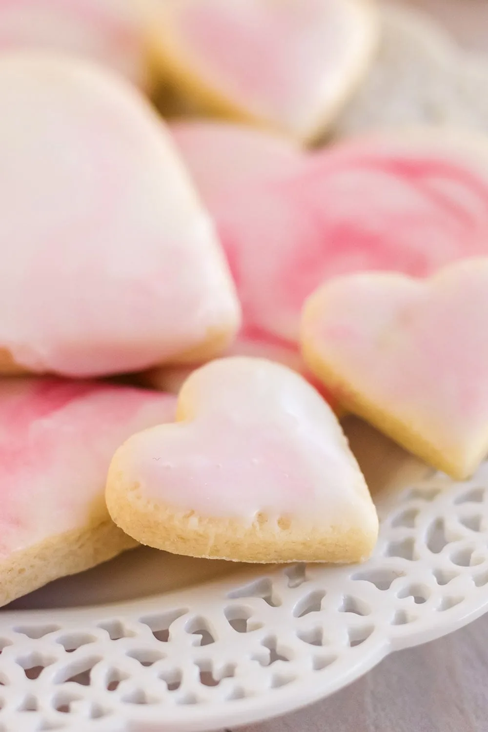 Plate of sugar cookies shaped into hearts with pink and white marble icing.