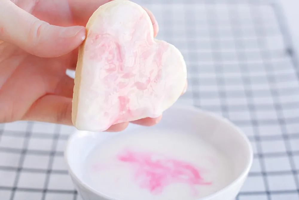 Dipping a heart cookie into pink and white icing.