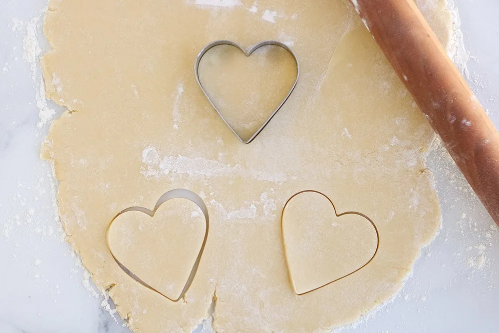 Cutting hearts out of sugar cookie dough with heart cookie cutter.