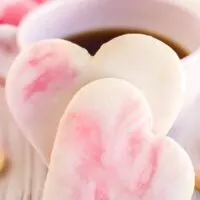 Two Valentine's day cookies in front of a cup of coffee.