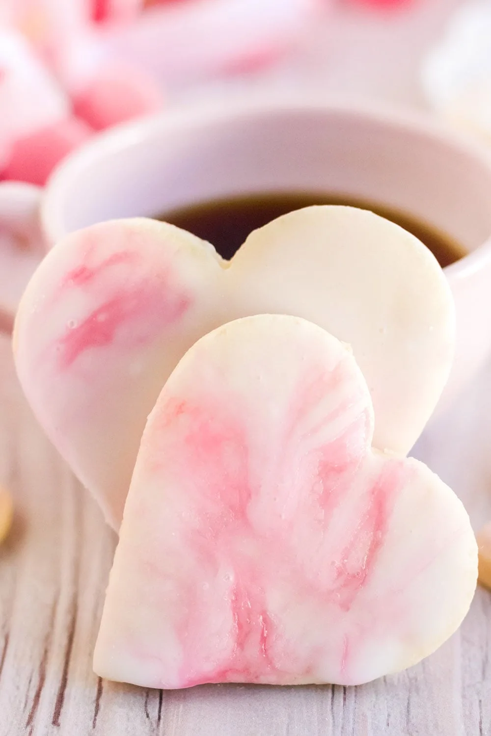 Two Valentine's day cookies in front of a cup of coffee.