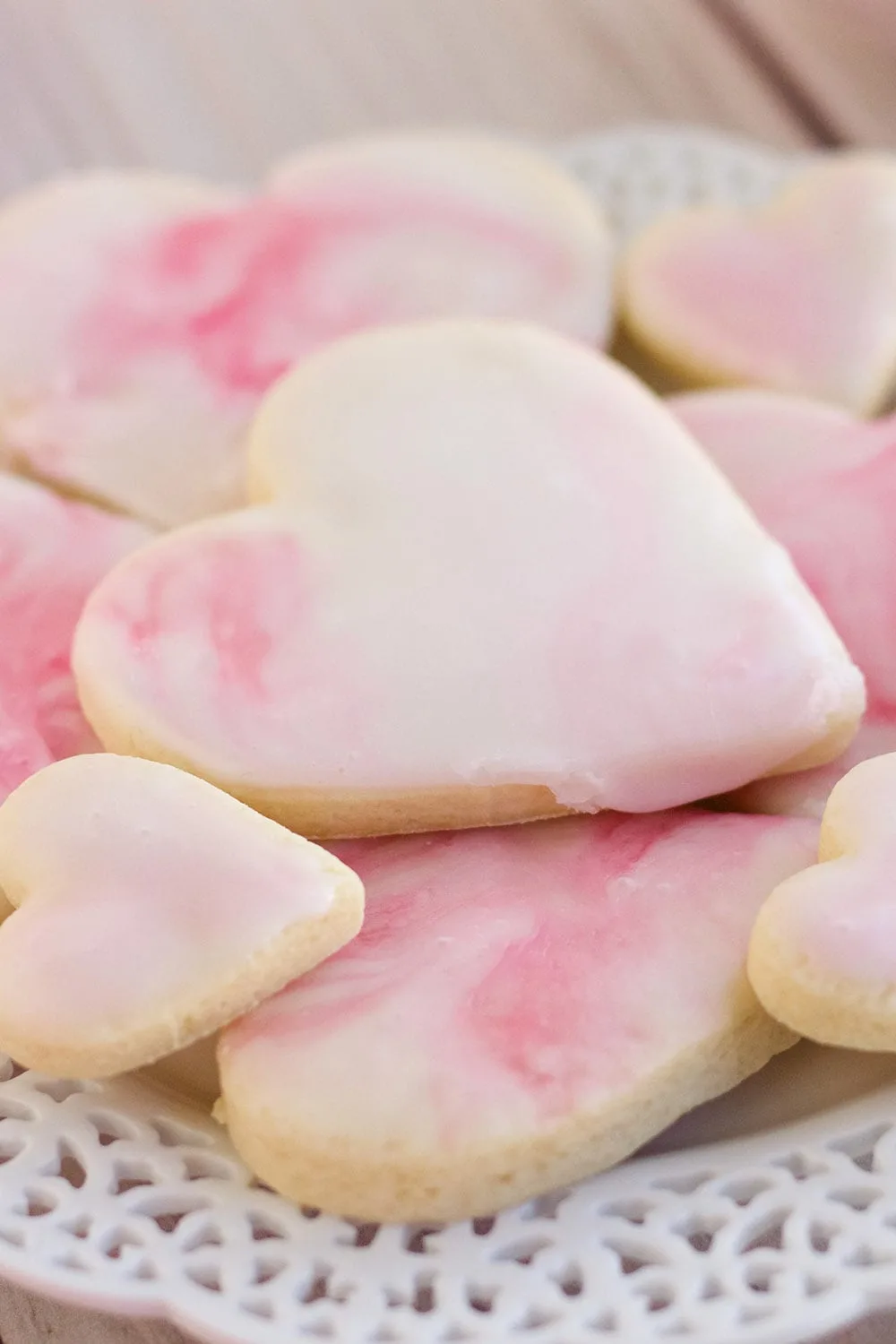 Pile of heart cookies with pink icing on a plate.