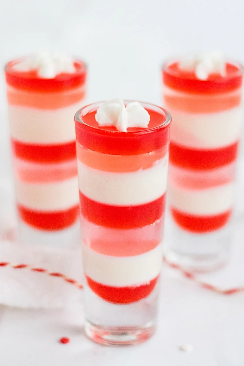 Three shooter glasses with layers of white, pink, and red gelatin.