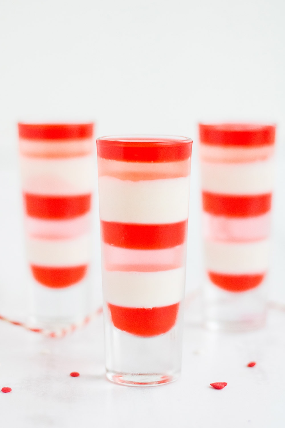 Three dessert shooters filled with red, white, and pink jello layers.