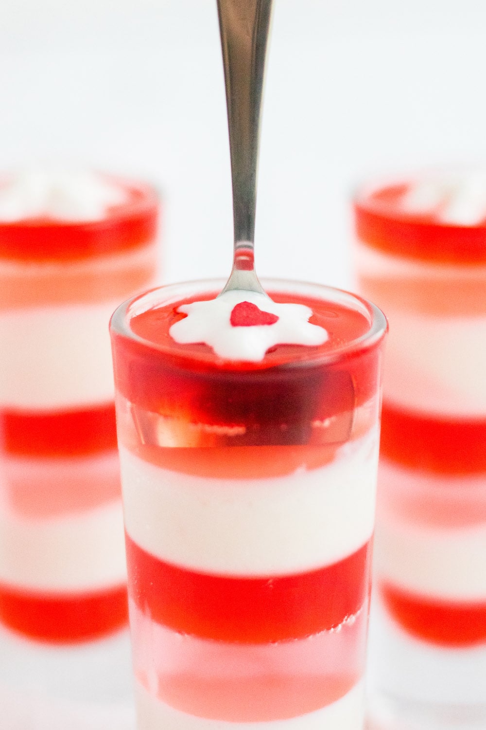 Spoon in a glass of layered jello with pink, red, and white layers.