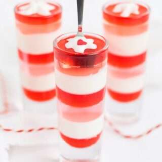 Three glasses of red, white, and pink layered jello. Tiny blobs of whipped cream top each one.