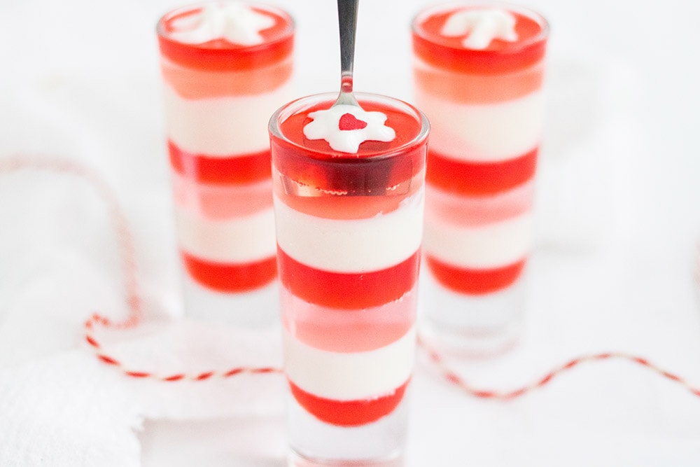 Three glasses of red, white, and pink layered jello. Tiny blobs of whipped cream top each one.