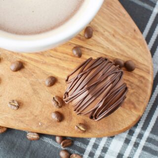 Mocha coffee bomb sitting next to a mug of coffee on a board with coffee beans.