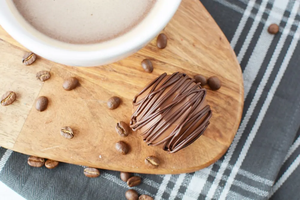 Mocha coffee bomb sitting next to a mug of coffee on a board with coffee beans.