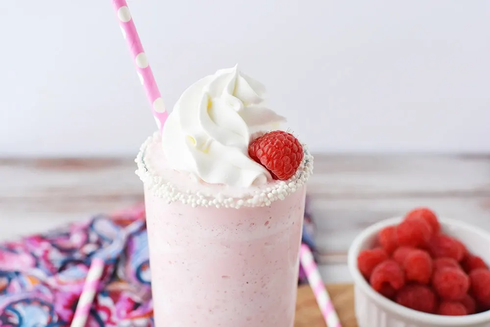 Glass of a pink raspberry blended drink with whipped topping and fresh raspberries. 