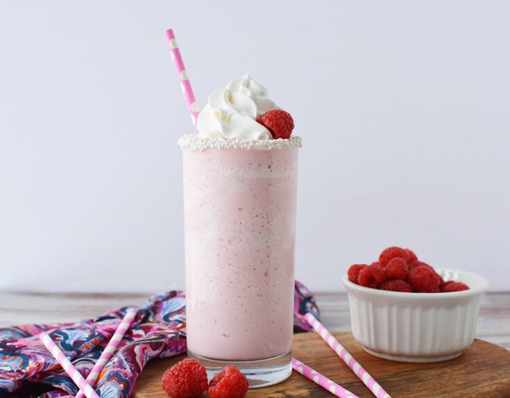 Pink cotton candy blended drink in a glass topped with whipped cream and raspberries.