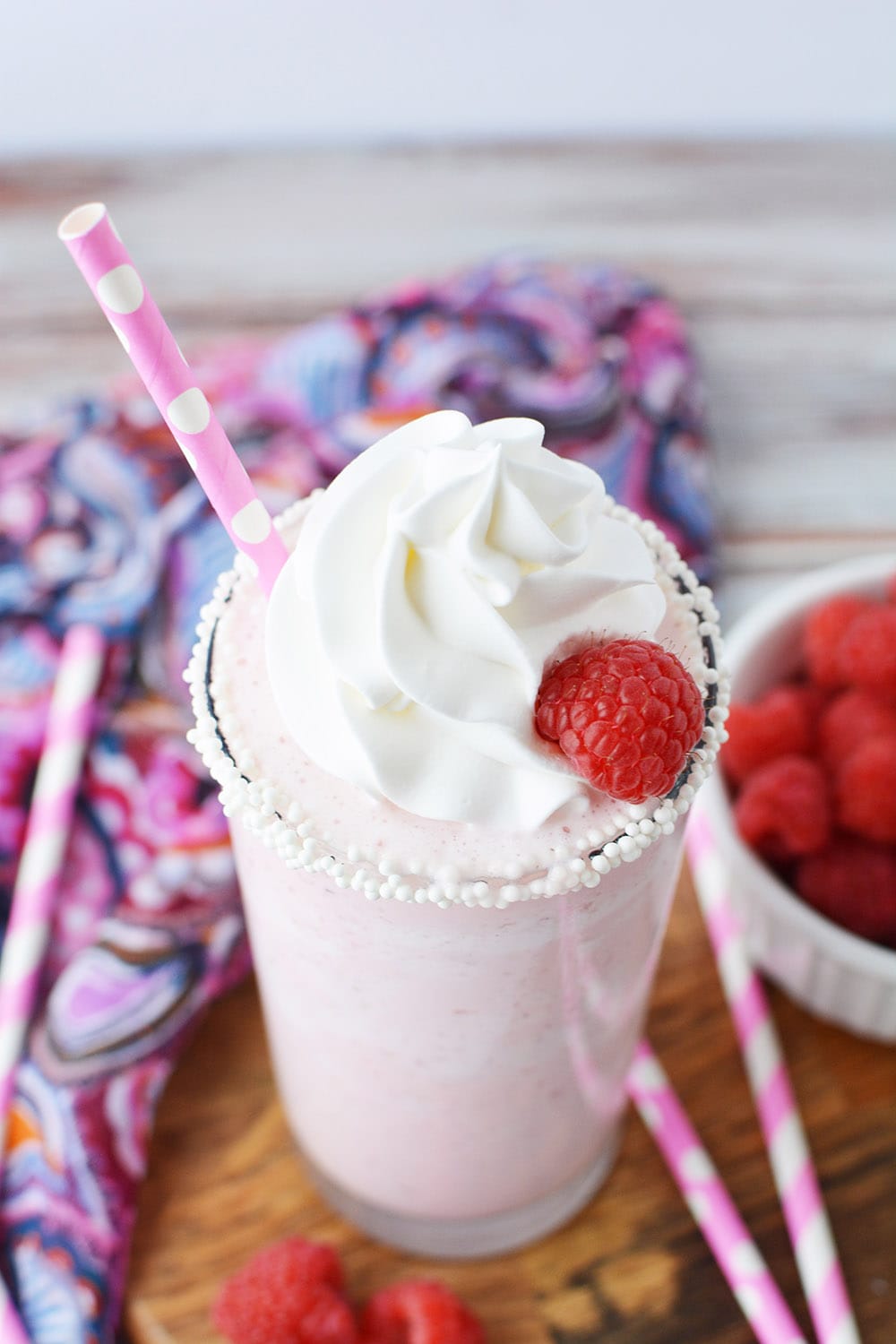 Tilted glass of raspberry frappe next to pink straws and fresh raspberries. 