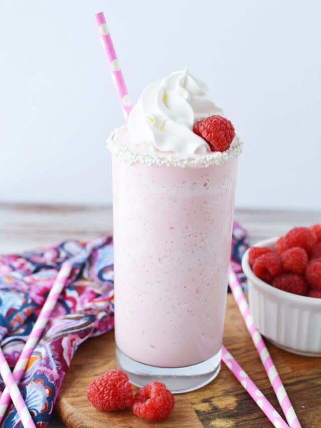 Glass of cotton candy frappuccino topped with whipped cream and raspberry and a pink straw.