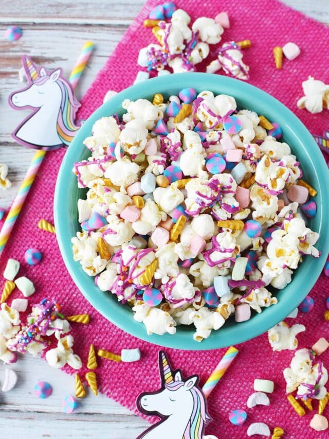 Bowl of unicorn party popcorn with party favors on table.