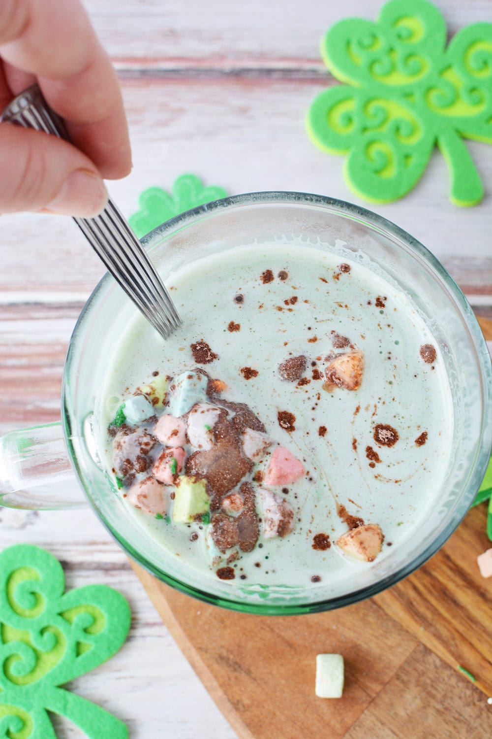Stirring green hot chocolate with rainbow marshmallows.