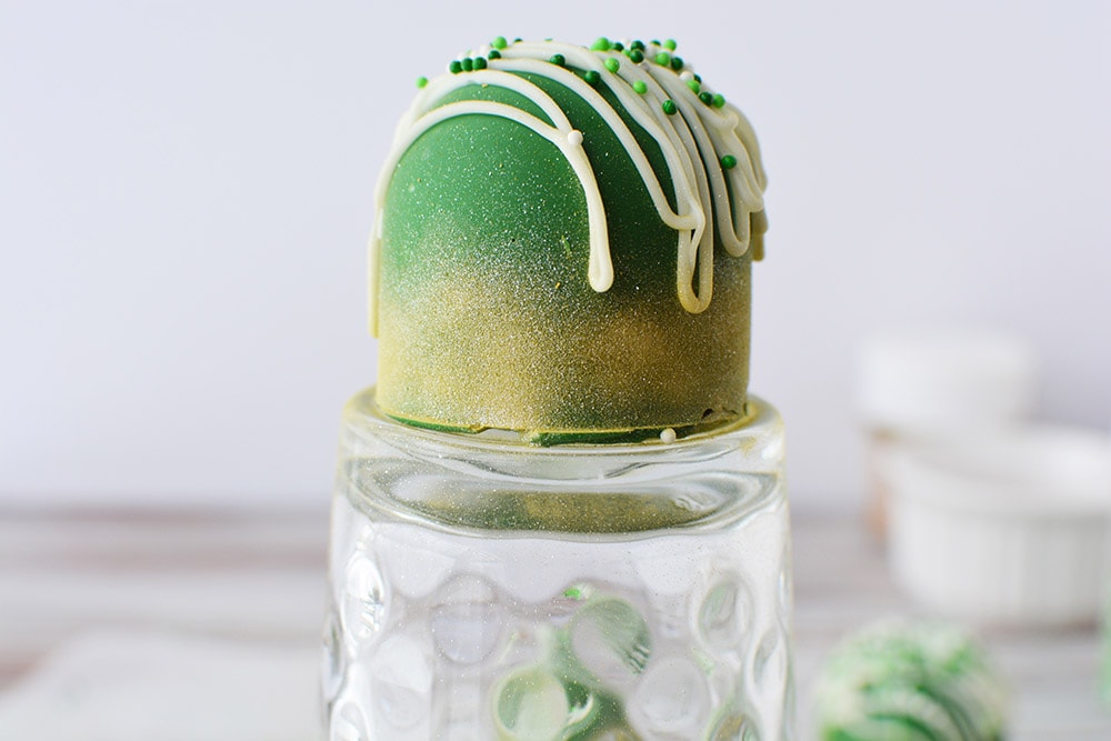 Green candy sitting on a glass after being sprayed with edible gold glitter spray.