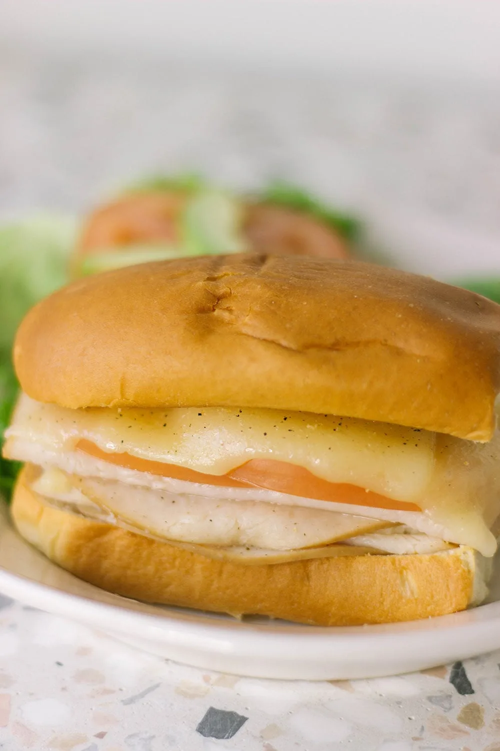 Turkey melt on a plate with lettuce and tomato in the background.