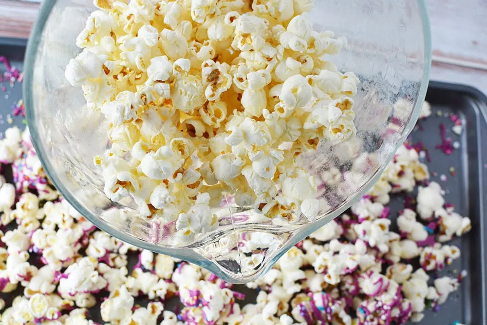 Bowl of popcorn over a baking sheet with more popcorn.