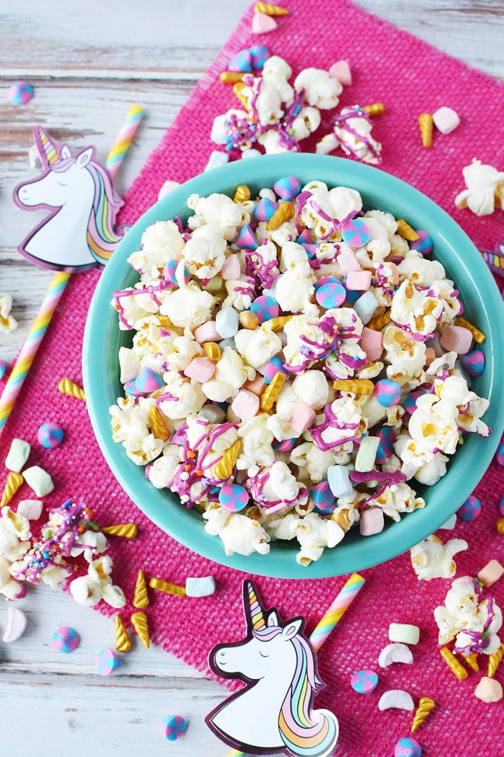 Bowl of unicorn party popcorn with party favors on table. 
