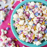 Unicorn popcorn in a bowl with more spilling out on the table.