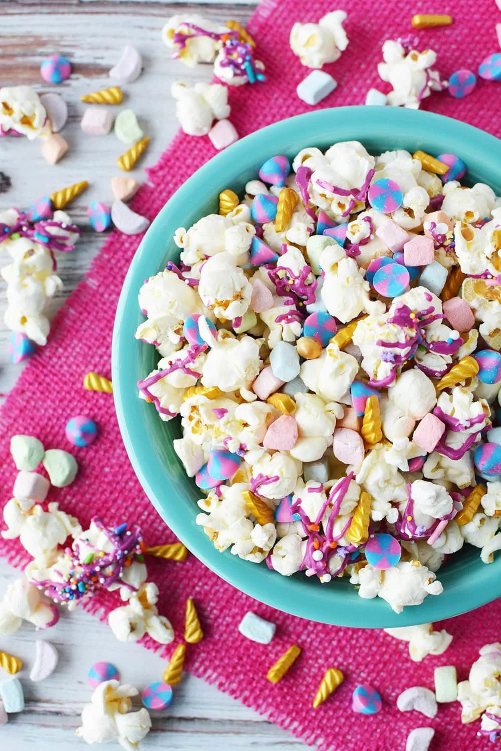 Unicorn popcorn in a bowl with more spilling out on the table. 