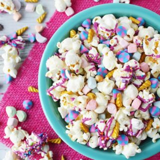 Blue bowl full of unicorn popcorn with popcorn and candies on table with a pink napkin.