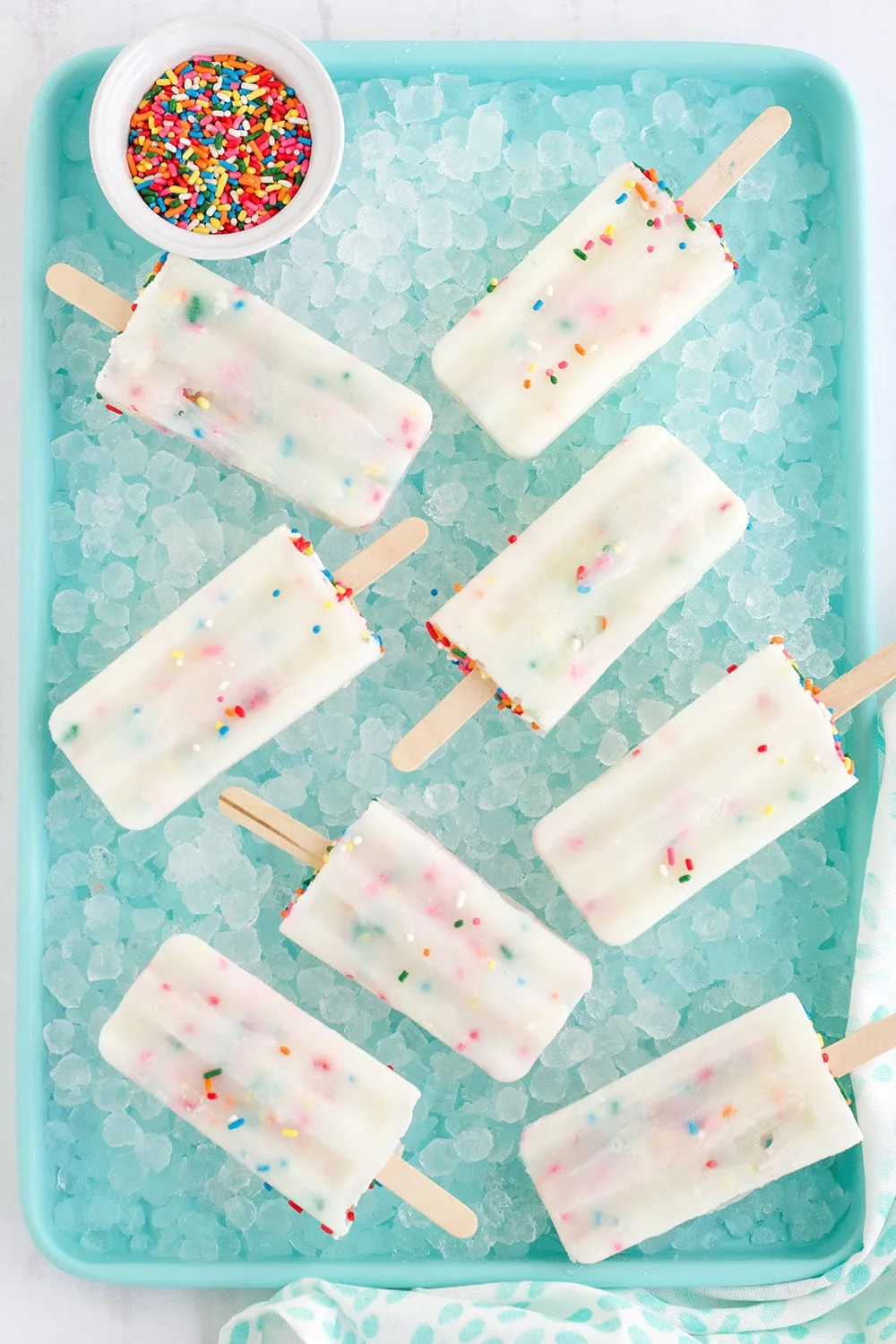 Several cake mix pops on a bed of ice in a blue tray.
