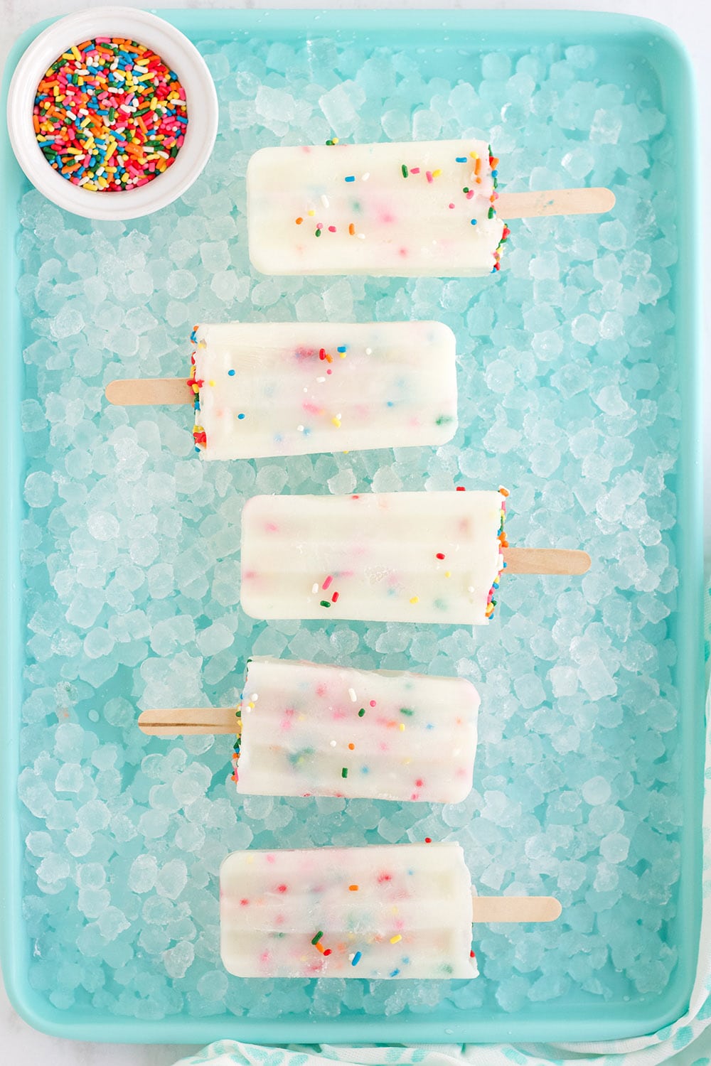 Cake batter pops in a row sitting on ice on a blue tray.