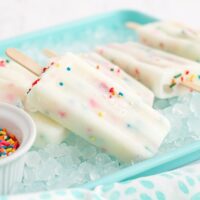 Cake batter popsicles laying on ice in a blue tray.