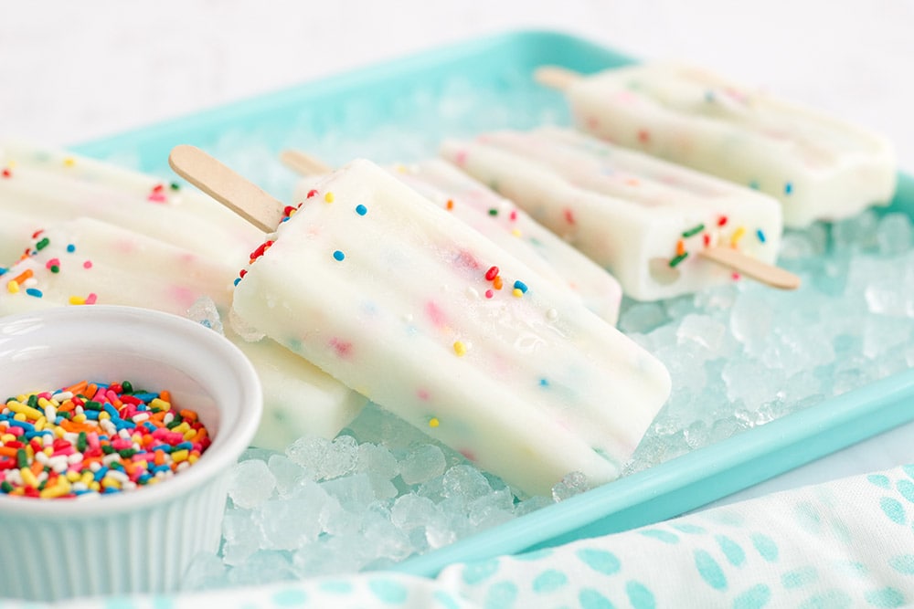 Cake batter popsicles laying on ice in a blue tray.