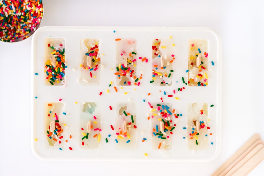 Sprinkles on top of popsicles in a freezing container.