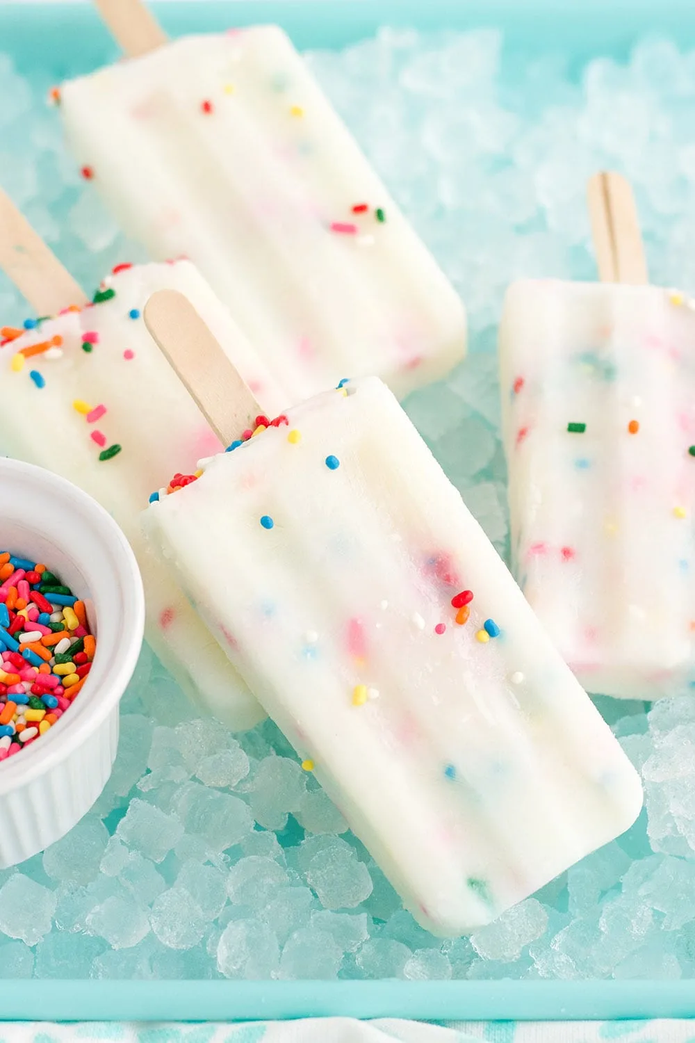 Cake popsicles laying on a bed of ice next to sprinkles.