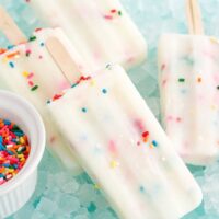 Cake popsicles laying on a bed of ice next to sprinkles.