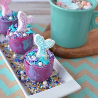 Mermaid hot chocolate melts on a plate next to a mug of hot chocolate. 