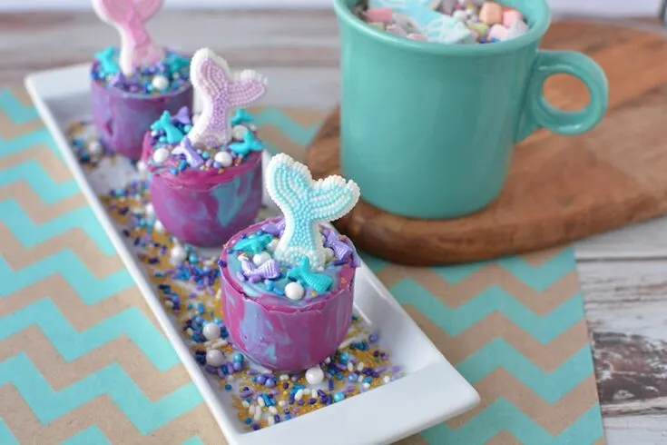 Mermaid hot chocolate melts on a plate next to a mug of hot chocolate. 