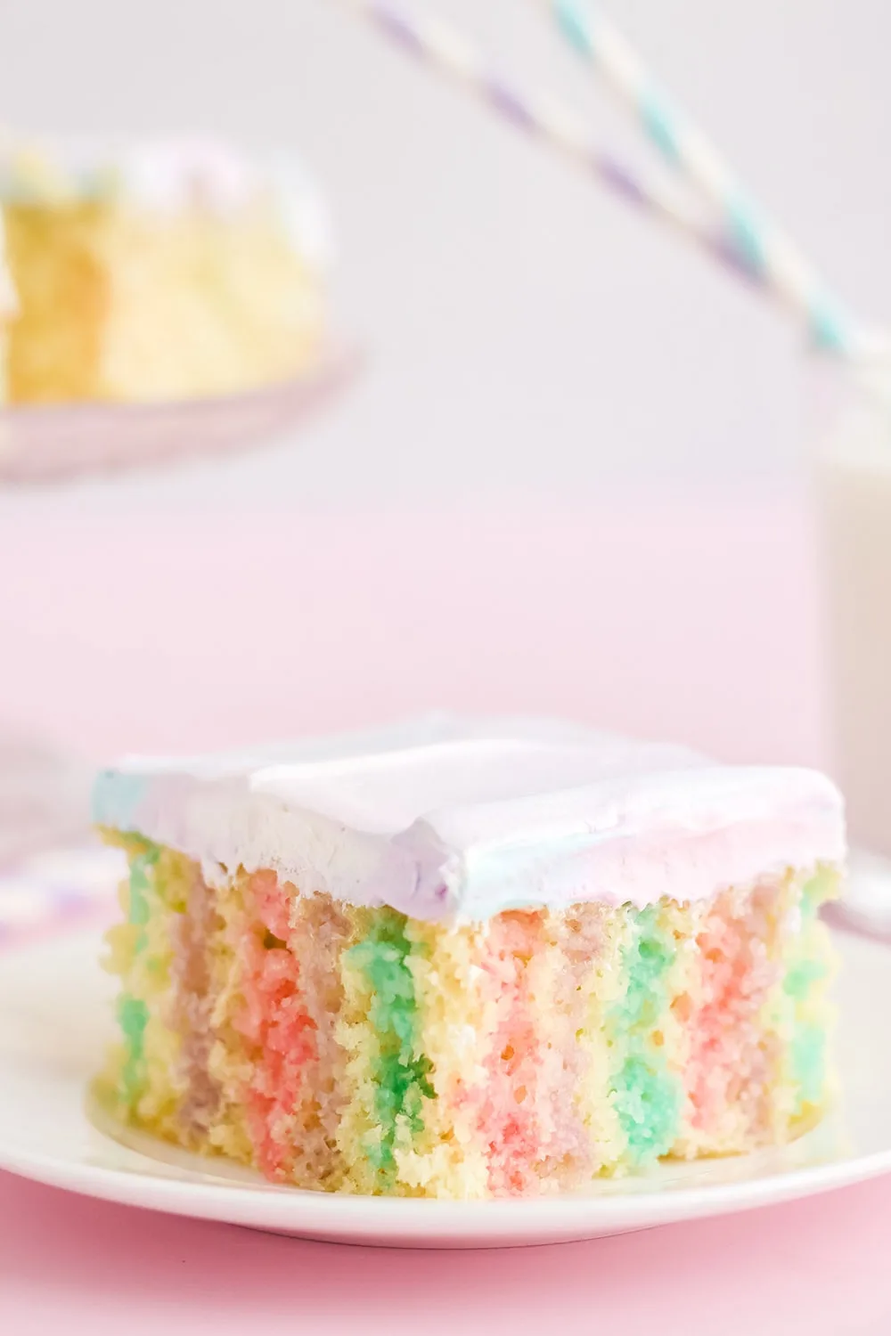 Unicorn poke cake on a plate with a pink background.