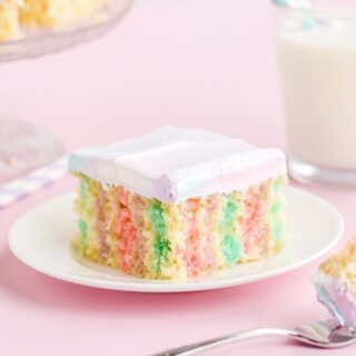 Rainbow poke cake on a white plate on a pink table with milk.