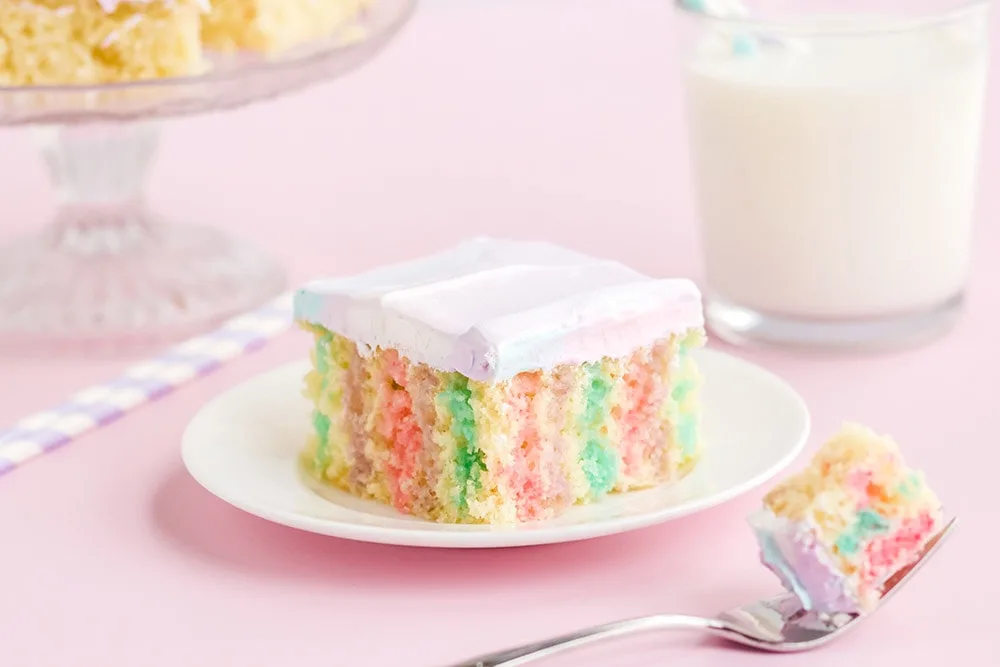 Rainbow poke cake on a white plate on a pink table with milk.