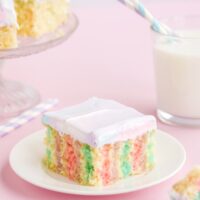 Colorful cake on a plate with milk and more cake in the background.